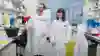 Dr Jamie Dean shows Curestarter Alice around the lab at University College London, Jamie is left wearing a lab coat and glasses Alice is on the right, and is also wearing a lab coat