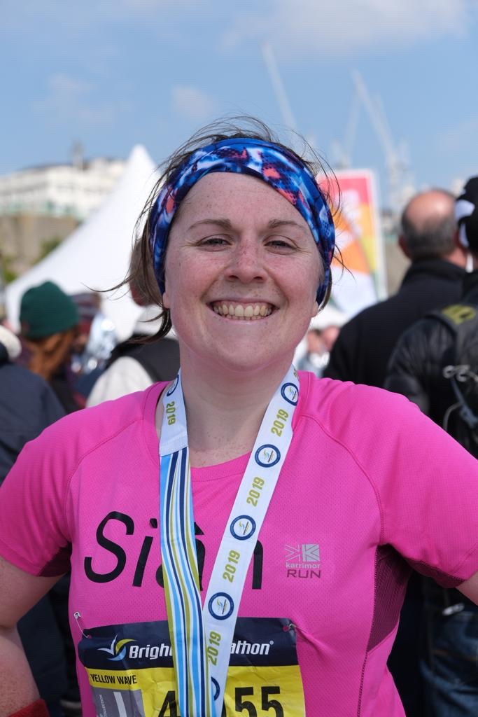 A smiling Sian looking directly at the camera wearing a hot pink running top and her medal for finishing the Brighton Marathon